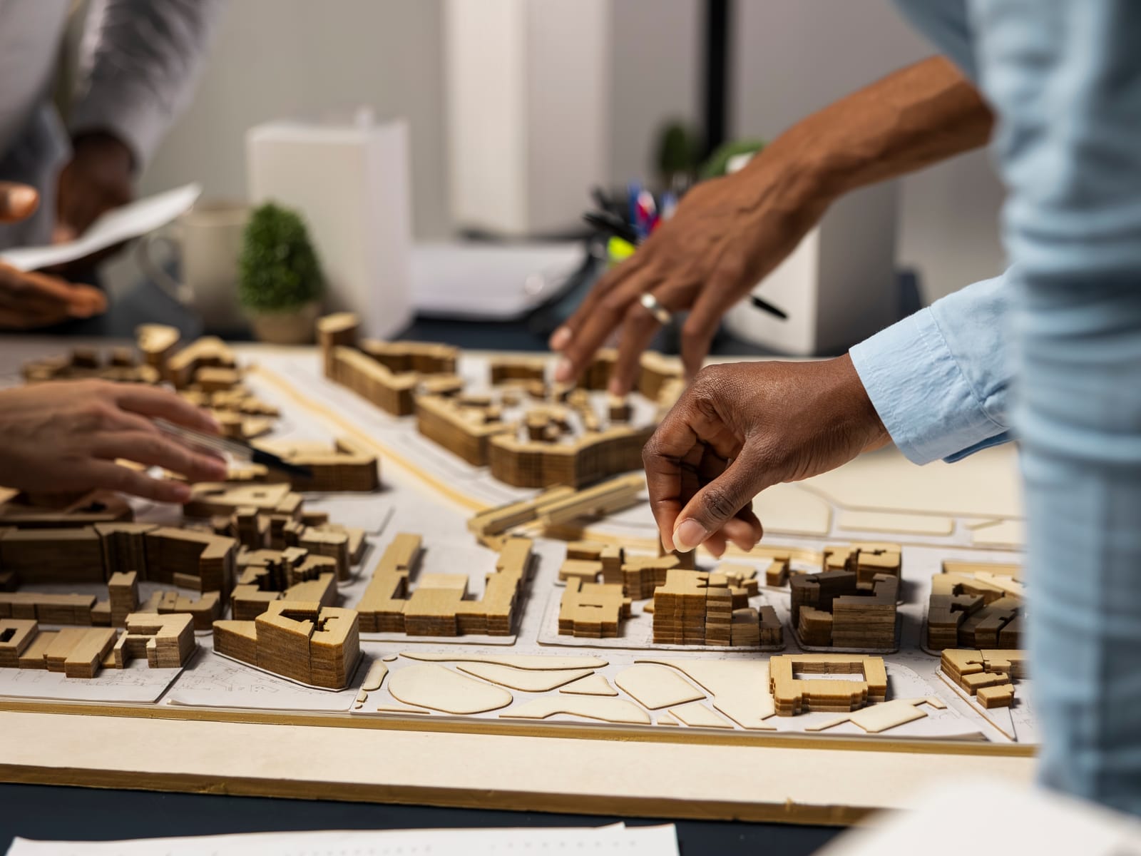 Hände über einem hölzernen Architekturmodell mit Gebäuderiegeln