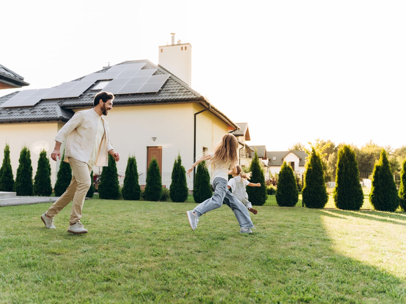 Familie spielt im Garten vor einem modernen Haus mit Solarmodulen